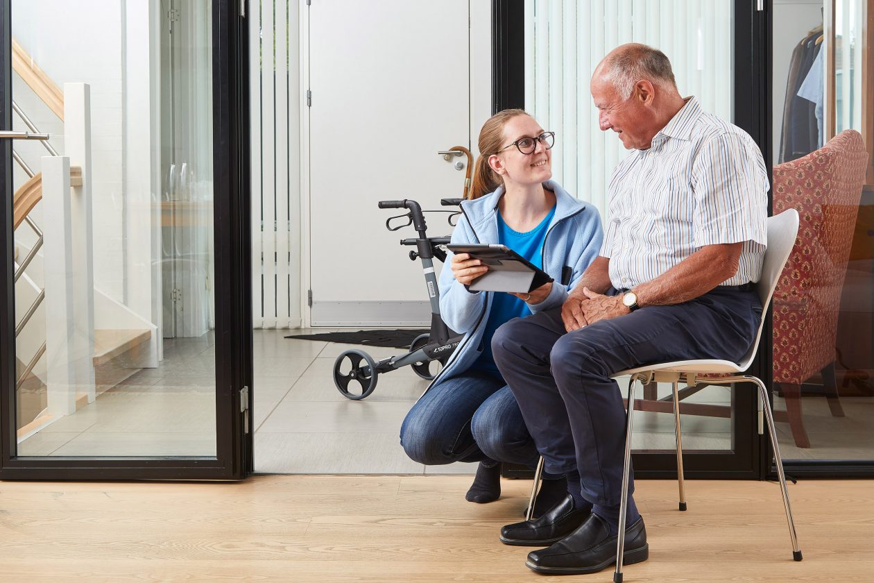 A care worker guides a client through an exercise, tablet in hand